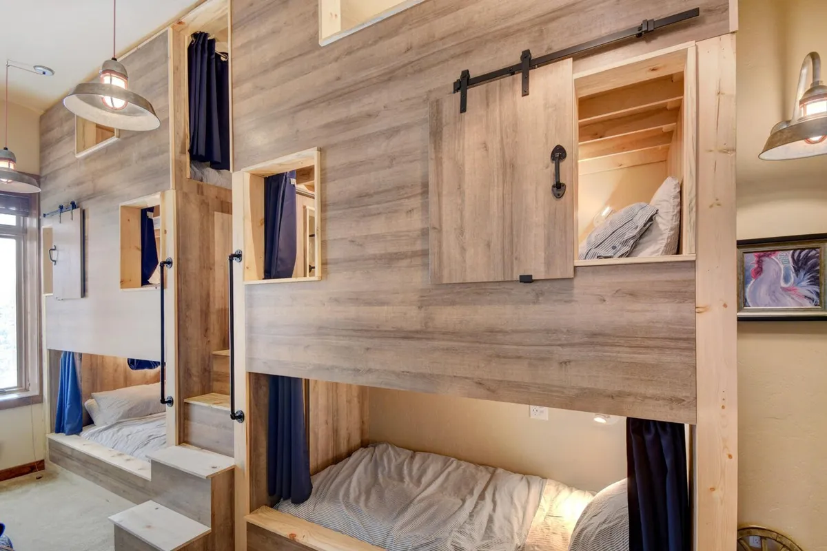 A whimsical bunkroom featuring custom-built triple bunk beds with six XL twin beds, surrounded by warm wooden textures, soft lighting, and playful curtains. The space feels both fun and cozy, designed for groups of kids or teens to share memorable nights.