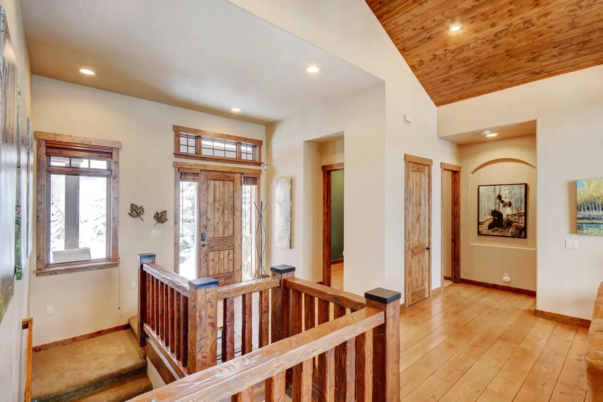 This image captures the home's entryway with a warm wooden railing, front door, wall art, and windows letting in natural light. The scene feels welcoming and highlights the initial impression guests receive upon arrival.