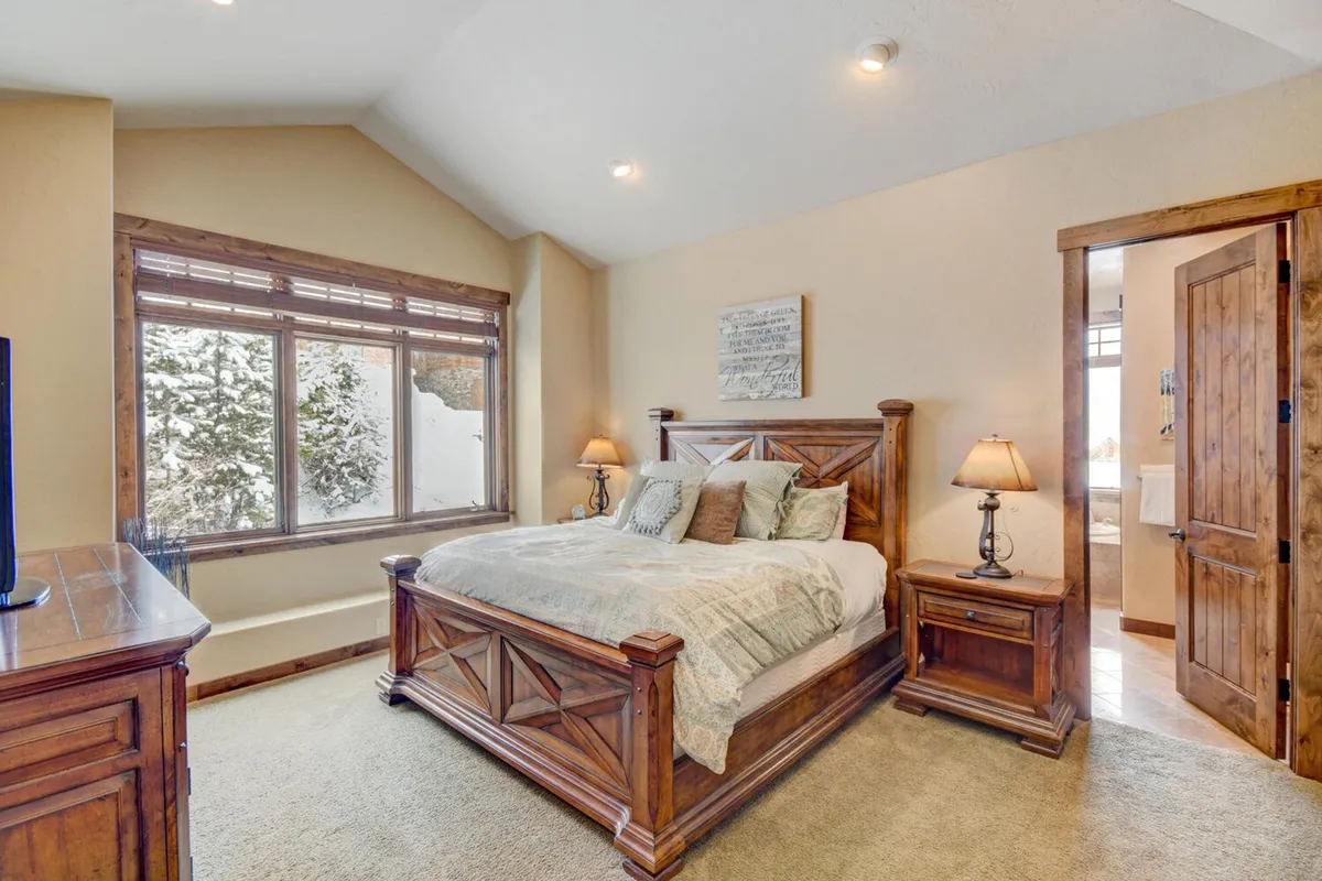 A serene king bedroom with a plush bed, large window bringing in natural light, a nightstand with a lamp, and a wooden dresser. The room exudes comfort, tranquility, and warmth—perfect for restful nights and refreshing mornings.