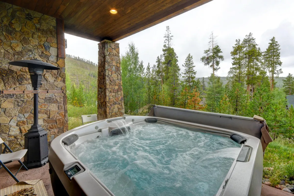 A tranquil outdoor hot tub nestled among stone columns and surrounded by nature, with inviting warm water and views of the landscape beyond. The setting suggests a perfect place to relax and unwind after an active day outdoors, whether in snow or sun.