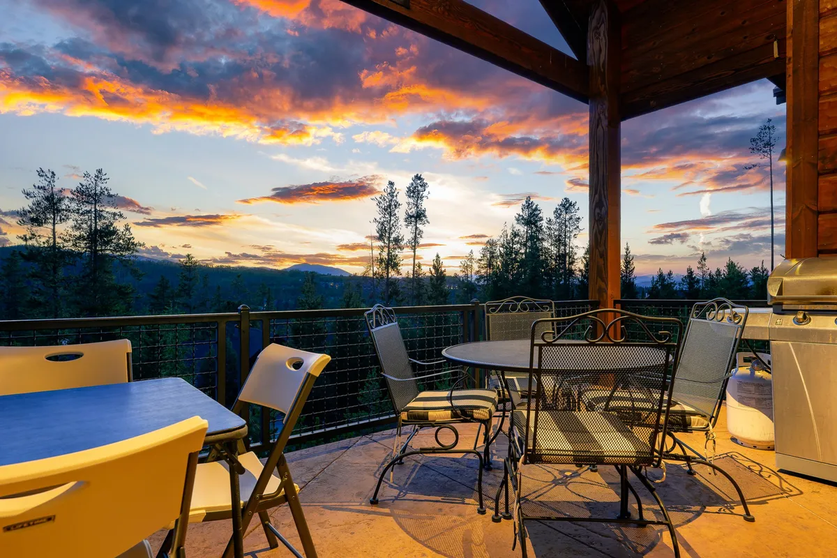 The image captures an outdoor dining set positioned to enjoy panoramic mountain views under a vibrant sunset sky. The relaxed mood suggests al fresco dinners, evening gatherings, and the creation of lasting memories under the stars.