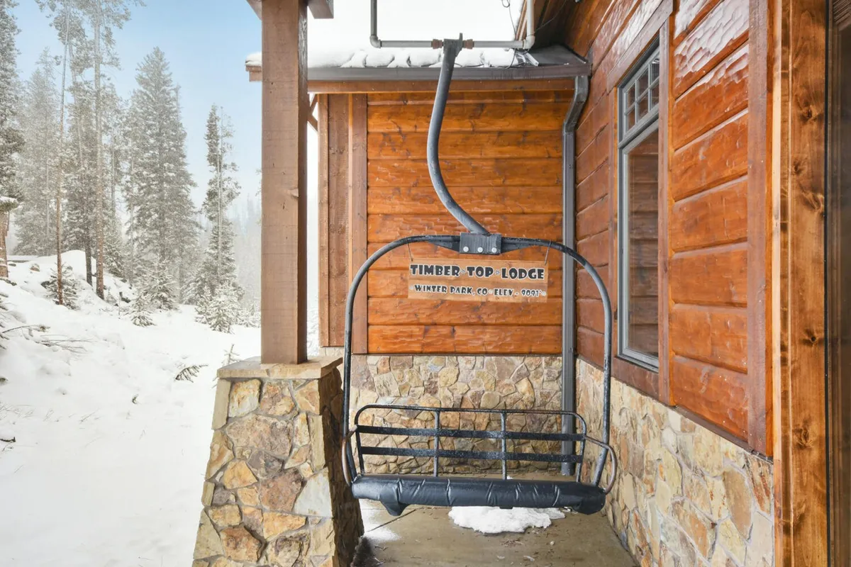 This exterior shot features a ski lift ascending over a snowy landscape, with a wooden lodge sitting atop a stone foundation. The background shows sunrise-painted snowy peaks, and the scene evokes the excitement of winter sports and alpine adventure.
