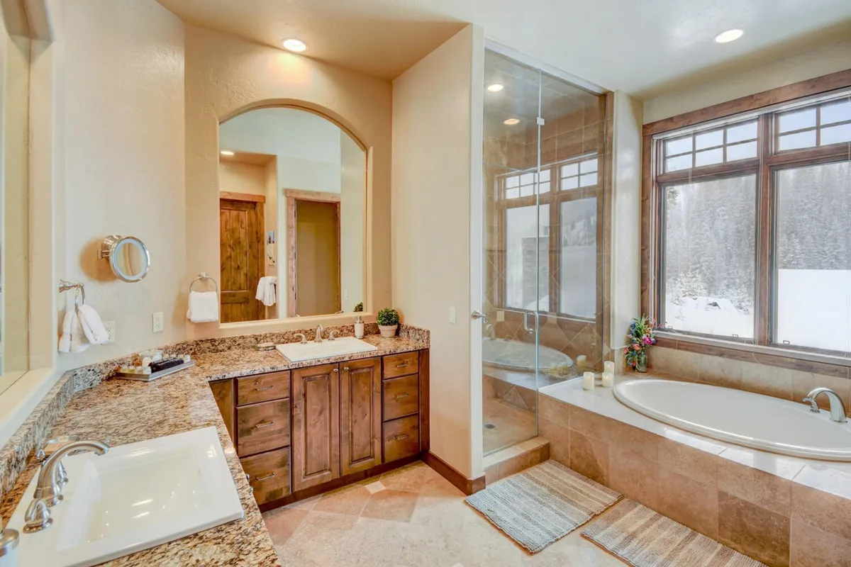 A luxurious spa-like bathroom featuring a large bathtub with a view of snowy landscape through expansive windows, granite countertops, and a well-appointed vanity area. The space feels calming and indulgent—ideal for unwinding after a day of adventure.